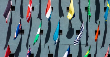 A photo of many flags for different countries, each hanging from a small window on a high wall