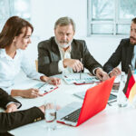 A group of diverse business professionals from different countries communicating with each other, with documents and laptops on the table.
