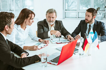 A group of diverse business professionals from different countries communicating with each other, with documents and laptops on the table.