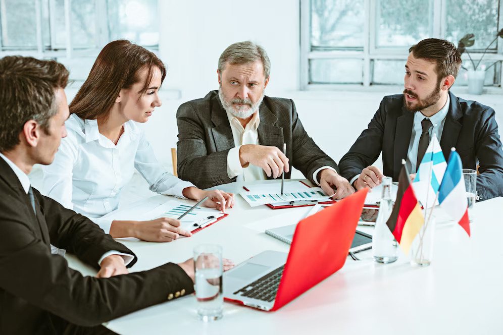 A group of diverse business professionals from different countries communicating with each other, with documents and laptops on the table.